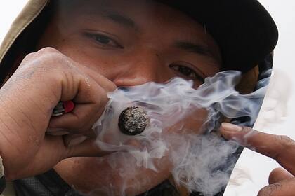 Un hombre fuma un cigarrillo de marihuana mientras participa en una marcha pidiendo la despenalización del uso recreativo del cannabis en Quito, Ecuador, el jueves 5 de mayo de 2022. (AP Foto/Dolores Ochoa)