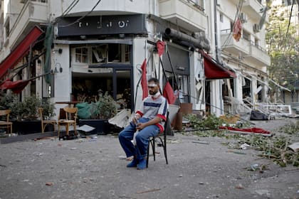 Un hombre herido se sienta al lado de un restaurante en el moderno barrio Mar Mikhael, de Beirut, que quedó destruido con la explosión de ayer