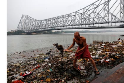 Un hombre limpia basura a lo largo de las orillas del río Ganges en Kolkata