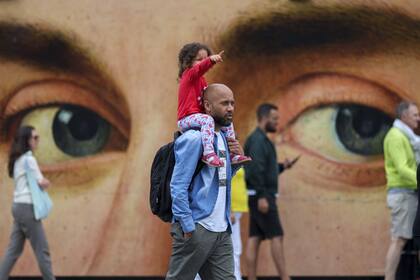 Un hombre lleva a una niña sobre sus hombros, caminando junto a un cartel que muestra una pintura del artista italiano Antonello da Messina afuera de la Galería Nacional en Trafalgar Square de Londres, el lunes 1 de julio de 2024.