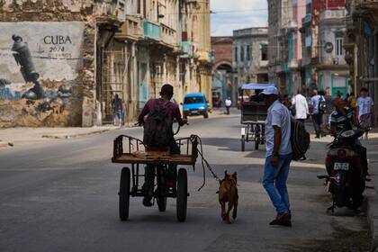Un hombre monta en triciclo con su perro atado con correa corriendo a su lado durante un apagón en La Habana
