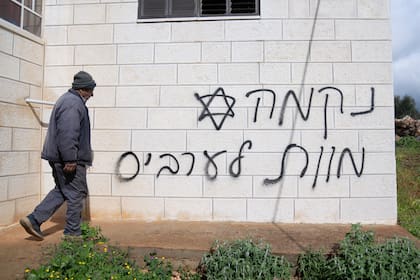 Un hombre pasa frente a una pared con un graffiti que dice en hebreo "venganza, muerte a los árabes", supuestamente pintado por colonos judíos en la aldea palestina de Turmus Ayya, en Cisjordania