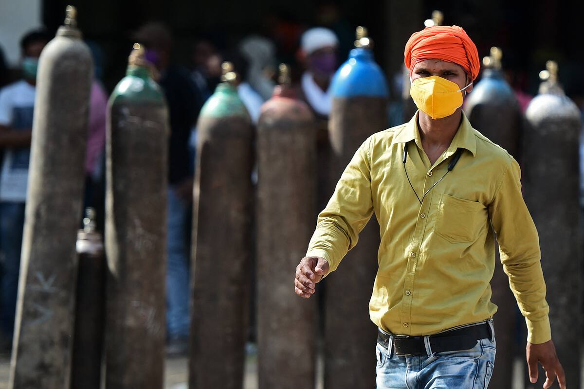Un hombre pasa junto a personas que esperan para rellenar sus cilindros de oxígeno médico para pacientes con coronavirus en una estación de recarga de oxígeno en Allahabad, la India, el 24 de abril de 2021