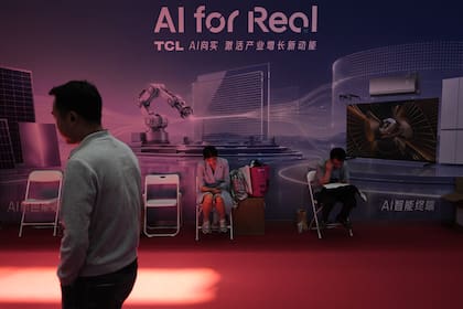 Un hombre pasa por delante de trabajadores descansando en un puesto de promoción de la Inteligencia Artificial