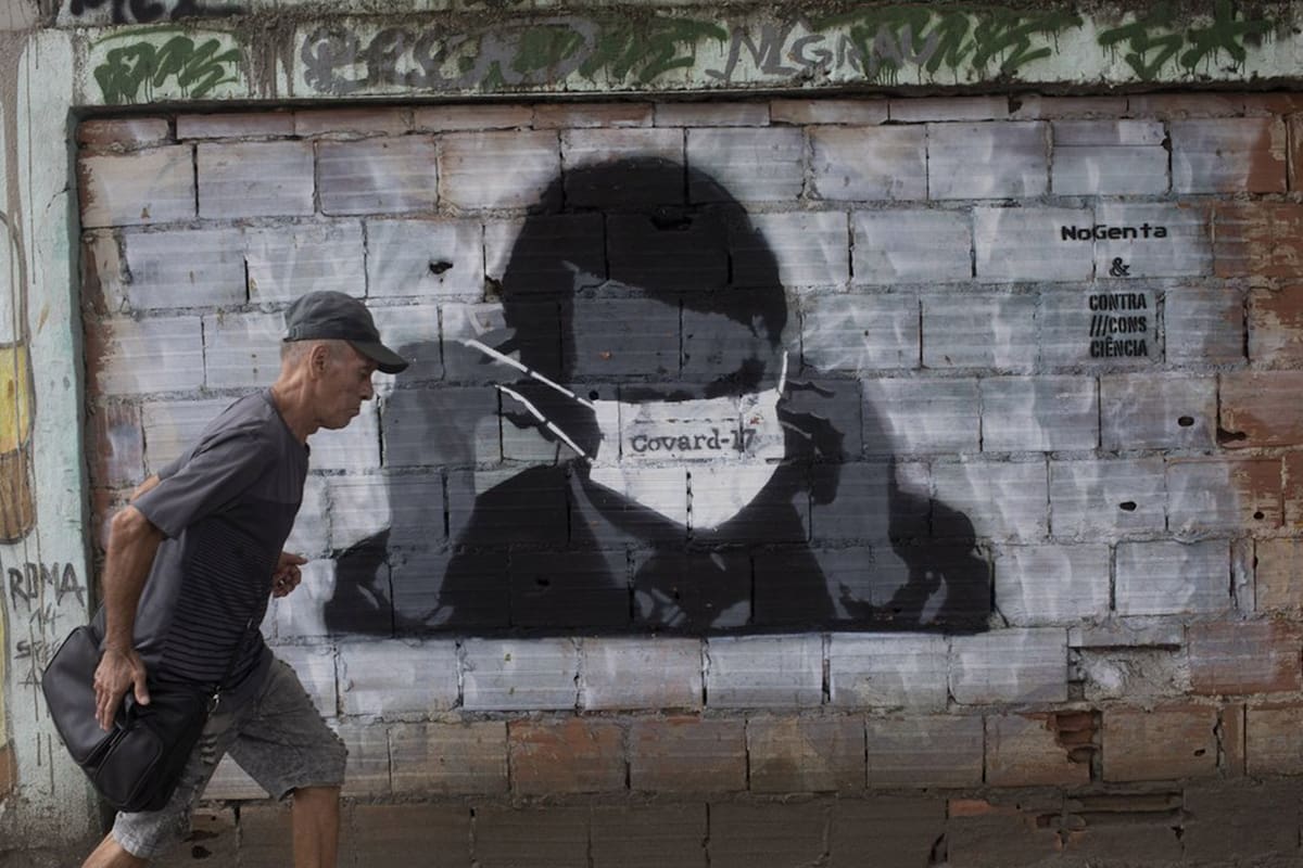 Un hombre pasa por delante de un mural con la imagen del presidente de Brasil, Jair Bolsonaro, colocándose una mascarilla con la palabra "cobarde" (en portugués) sobre los ojos, en Río de Janeiro