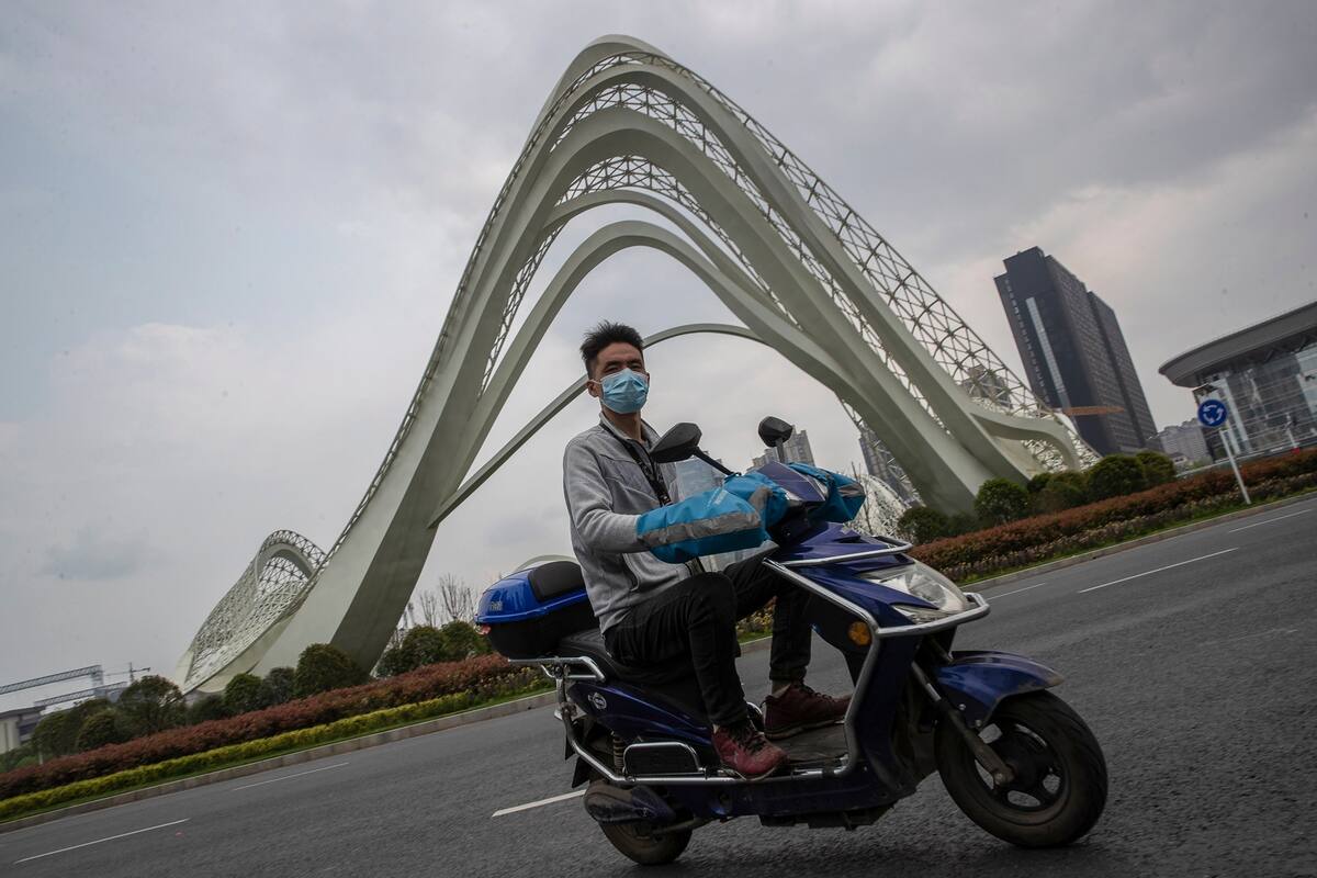 Un hombre que lleva un barbijo mientras conduce un scooter en Wuhan, en la provincia central china de Hubei. - China levantó las duras restricciones a la provincia en el epicentro del brote de coronavirus el 25 de marzo después de un cierre de meses, ya que el país no informó de nuevos casos interno