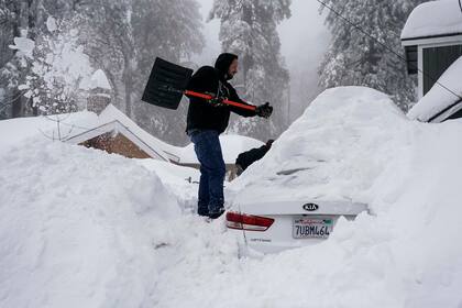 Un hombre retira la densa capa de nieve sobre su automóvil en Running Springs, California