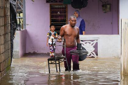 Un hombre se lleva una silla y un ventilador de su casa inundada en Tumpat, Malasia, el martes 3 de diciembre de 2024. (AP Foto/Vincent Thian)