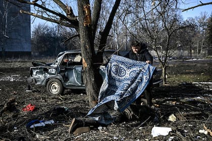 Un hombre usa una alfombra para tapar un cadáver en Chuguev, en el este de Ucrania, tras los bombardeos rusos. (Photo by Aris Messinis / AFP)