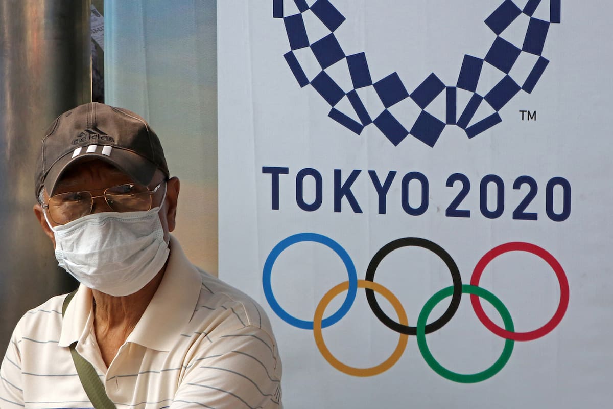 Un hombre usa una máscara higiénica mientras se sienta junto a un anuncio para promocionar los Juegos Olímpicos de Tokio 2020 en la parada de autobús en Bangkok el 05 de febrero de 2020