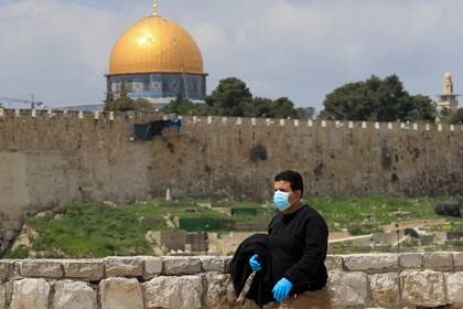 Un hombre vestido con una máscara y guantes pasa junto a la mezquita de la Cúpula de la Roca en la Ciudad Vieja de Jerusalén el 2 de abril de 2020
