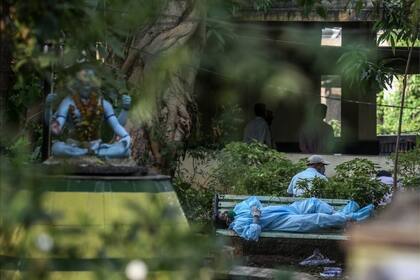 Un hombre vestido en traje protector descansa en un banco antes de realizar los ritos fúnebres a un familiar víctima de coronavirus, en Bombay