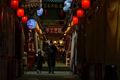 Un hombre y un niño con cubrebocas caminan entre tiendas cerradas el 3 de enero de 2023, en Qianmen, un popular destino turístico en Pekín. (AP Foto/Andy Wong, Archivo)