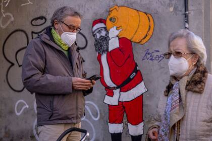 Un hombre y una mujer, con mascarillas FFP2 para frenar la propagación del coronavirus, delante de un mural que representa a Papá Noel, En Madrid, el 12 de enero de 2022. (AP Foto/Manu Fernández)