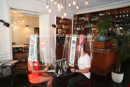 Un hombre y una mujer demuestran cenar bajo un escudo de plástico el miércoles 27 de mayo de 2020 en un restaurante de París. A medida que los restaurantes en Francia, amante de la comida, se preparan para reabrir, algunos invierten en escudos de plástico con forma de pantalla para proteger a los co