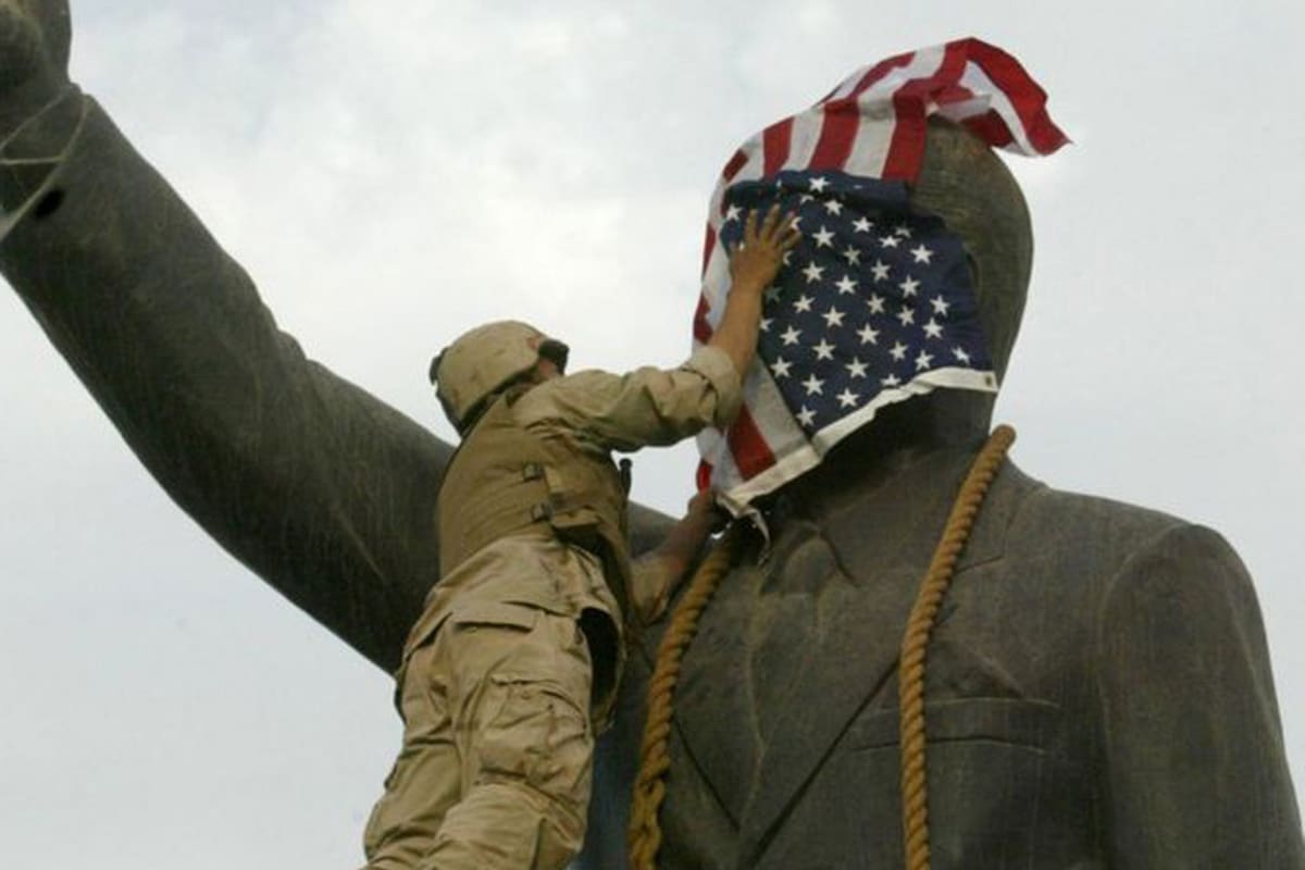 Un infante de marina estadounidense cubre el rostro de la estatua de Saddam Hussein en Bagdad días después de la invasión. La estatua luego fue derribada, convirtiéndose en una símbolo del derrocamiento del líder iraquí.