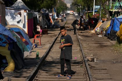 Un joven migrante venezolano juega en las vías del tren bordeadas de tiendas de campaña en la Ciudad de México