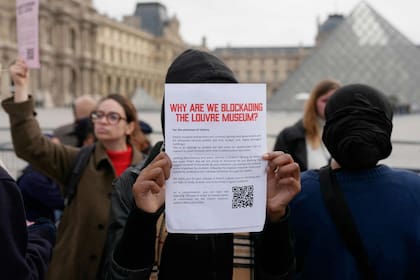 Un joven muestra un cartel que informa a los visitantes sobre el cierre, mientras manifestantes, entre ellos estudiantes de la Escuela del Louvre, bloquean la entrada al Museo del Louvre para expresar su apoyo al movimiento estudiantil