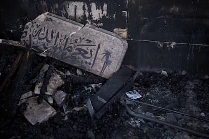 Un letrero dañado, que muestra parte de un versículo del Corán con la frase en árabe "Llas mezquitas de Alá serán mantenidas", yace en el suelo a la entrada de una mezquita incendiada durante un ataque de colonos israelíes