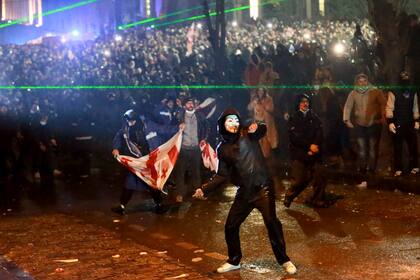 Un manifestante enmascarado lanza un objeto hacia la policía durante una protesta el domingo 1 de diciembre de 2024, afuera del Parlamento en Tiflis, Georgia, contra la decisión del gobierno para suspender las negociaciones para que la nación se incorpore a la Unión Europea. (AP Foto/Zurab Tsertsvadze)