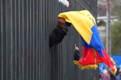 Un manifestante indígena lleva una bandera ecuatoriana dentro de la Casa de la Cultura en Quito mientras policías fuerzan a los manifestantes a quedarse adentro durante una protesta contra el gobierno del presidente Guillermo Lasso