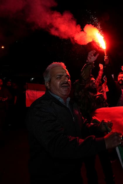 Un manifestante iraní enciende una bengala mientras otros portan una bandera palestina durante una reunión antiisraelí en la plaza Felestin (Palestina). en Teherán, Irán