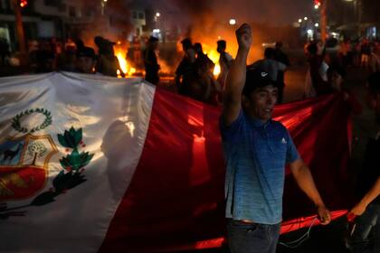 Un manifestante lanza proclamas contra el gobierno mientras otros llevan una bandera nacional durante el bloqueo de la autopista Panamericana Norte en Chao, Perú, el viernes 17 de febrero de 2023. (AP Foto/Martín Mejía)