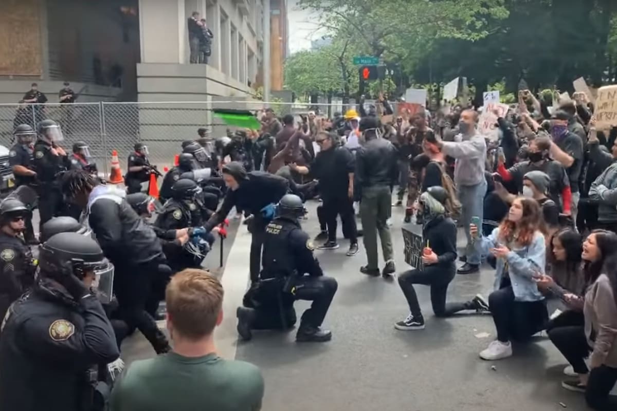 Un manifestante le da la mano a un policía arrodillado, en medio de una protesta contra la violencia racial en Portland (Ryan Ao)