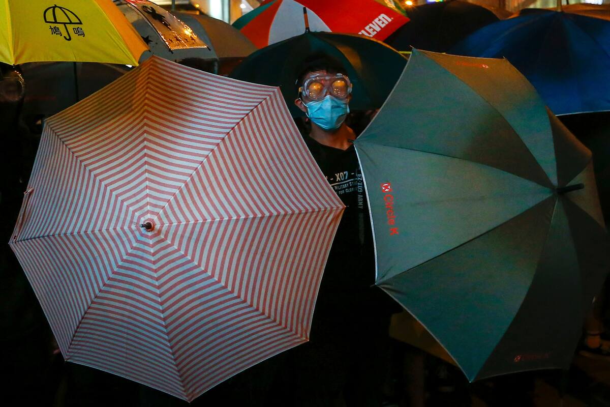 Un manifestante observa a la policía escudándose tras dos paraguas, anteayer, durante una protesta en Hong Kong