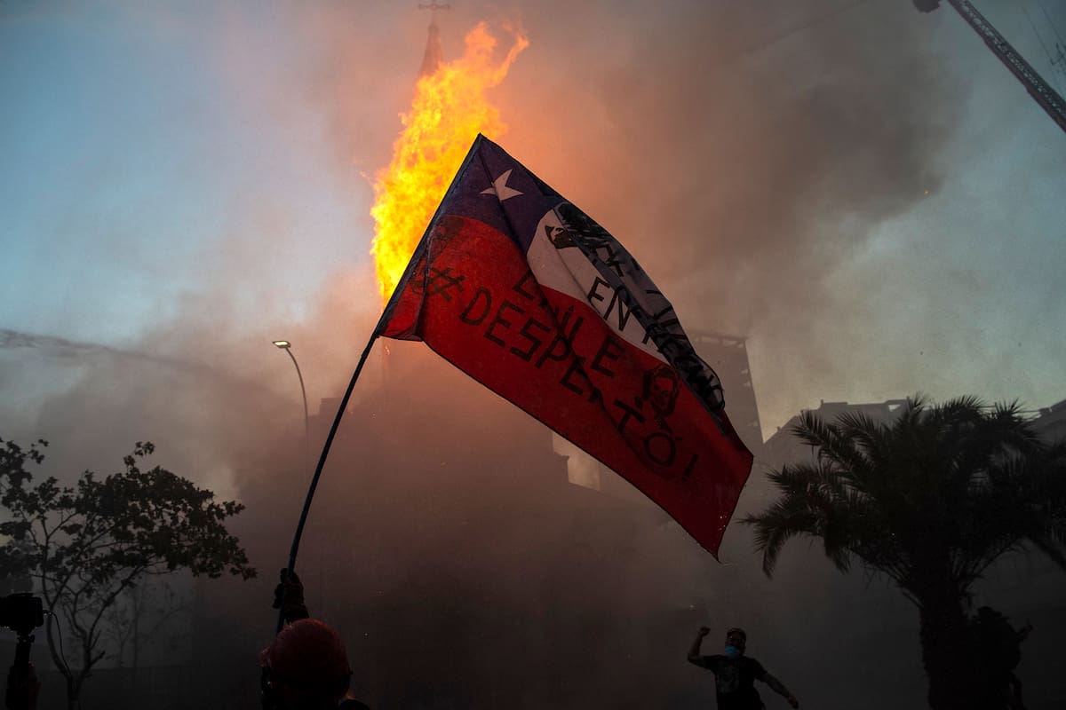 Un manifestante ondea una bandera chilena frente a la iglesia en llamas de Asunción, en la conmemoración del primer aniversario del levantamiento social en Chile, en Santiago, el 18 de octubre de 2020, mientras el país se prepara para un referéndum histórico