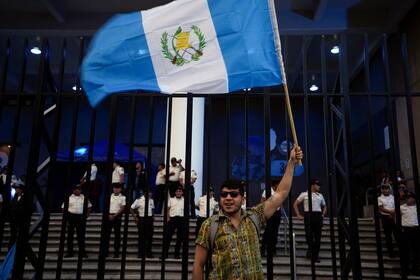 Un manifestante ondea una bandera guatemalteca frente al edificio de la oficina del Fiscal General para mostrar su apoyo al proceso electoral y al avance de la segunda vuelta de las elecciones presidenciales en Ciudad de Guatemala, el viernes 14 de julio de 2023. (Foto AP/Moisés Castillo)