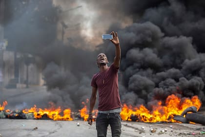 Un manifestante se toma una selfie en una barricada en llamas, el lunes 18 de octubre de 2021, en Puerto Príncipe, Haití. (AP Foto/Joseph Odelyn)