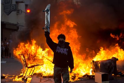 Un manifestante sostiene una patineta frente a un incendio en Los Ángeles, el sábado 30 de mayo de 2020, durante una protesta por la muerte de George Floyd