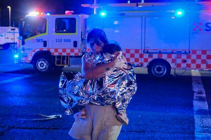Un miembro del público abandona la escena con su hijo, que está cubierto con una manta de emergencia, después de un tiroteo en Bondi Beach el 14 de diciembre de 2025 en Sídney, Australia