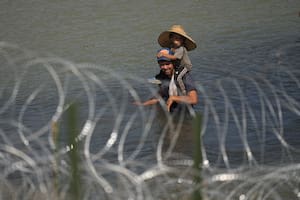 Un migrante cruza el río Bravo con un niño sobre sus hombros en un intento por llegar a Estados Unidos desde México, cerca del lugar donde trabajadores instalan una fila de boyas para que sean una barrera flotante, el martes 11 de julio de 2023, en Eagle Pass