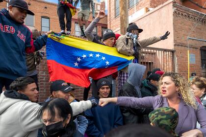 Un migrante de varios, a la izquierda, choca el puño con una residente local que los apoya en el centro de El Paso, Texas, el sábado 7 de enero de 2023. Al fondo varios migrantes muestran una bandera venezolana. (AP Foto/Andres Leighton)
