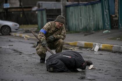 Un militar revisa el cuerpo de un civil en Bucha
