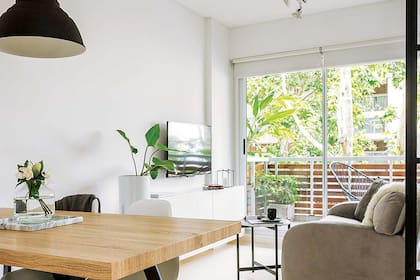 Un mueble poco profundo le da marco al living. Adentro tiene estantes inclinados para guardar los zapatos. Sillas ‘Eames’ y mesa con tapa de roble y base de hierro (Tienda Vainilla). Bandeja de mármol arabescato (VK Home). Florero de vidrio (Organizza).