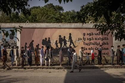 Un mural de advertencia contra la migración sirvió de telón de fondo para las personas que hacían cola frente a la oficina de pasaportes en Kabul.