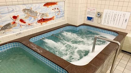 Un mural de porcelana Kutani de carpas koi se encuentra encima de una de las bañeras de Konparu-yu