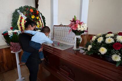 Un nieto se sostiene sobre el ataúd abierto que contiene los restos de su abuelo, el periodista asesinado Armando Linares, en Zitácuaro, en el estado de Michoacán, México, el miércoles 16 de marzo de 2022.  (AP Foto/Marco Ugarte)