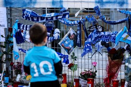 Un niño con la camiseta número 10 del Napoli se detiene junto a los recuerdos de la leyenda del fútbol Diego Armando Maradona abandonados en la valla del estadio San Paolo en Nápoles, Italia, el jueves 26 de noviembre de 2020. Maradona murió el miércoles 25 de noviembre de 2020.