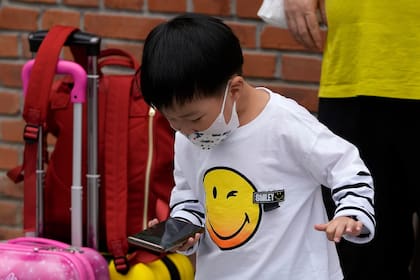 Un niño, con mascarilla por la pandemia del coronavirus, juega en un smartphone cerca de un familiar, en Beijing, el 12 de septiembre de 2021. (AP Foto/Andy Wong)