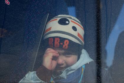 Un niño mira a través de la ventana de un autobús en el que viajan refugiados que huyen de la invasión rusa de Ucrania, en la localidad fronteriza de Przemysl, en Polonia, el 26 de febrero de 2022 (AP Foto/Petr David Josek)