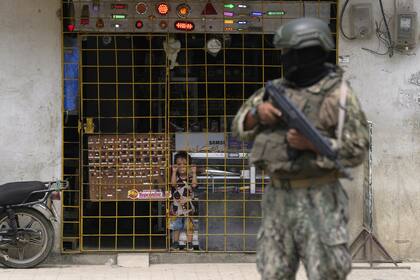 Un niño mira desde detrás de la puerta de un comercio tienda mientras un soldado realiza una guardia de seguridad