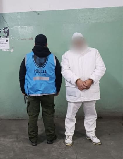 Un oficial de la Policía de la Ciudad escolta a uno de los empleados detenidos, esposado y vestido con la ropa de trabajo