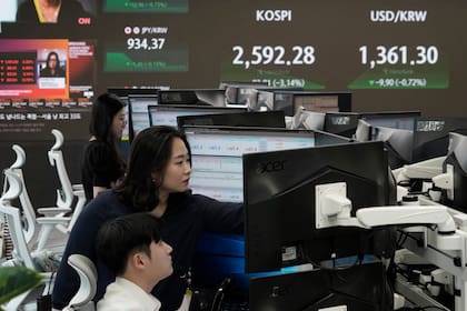 Un operador de divisas trabaja junto a una pantalla que muestra el Korea Composite Stock Price Index (KOSPI), a la izquierda, y la tasa de cambio entre el dólar estadounidense y el won surcoreano en el patio de operaciones de la sede de KEB Hana Bank en Seúl, Corea del Sur, el lunes 5 de agosto de 2024. (AP Foto/Ahn Young-joon)