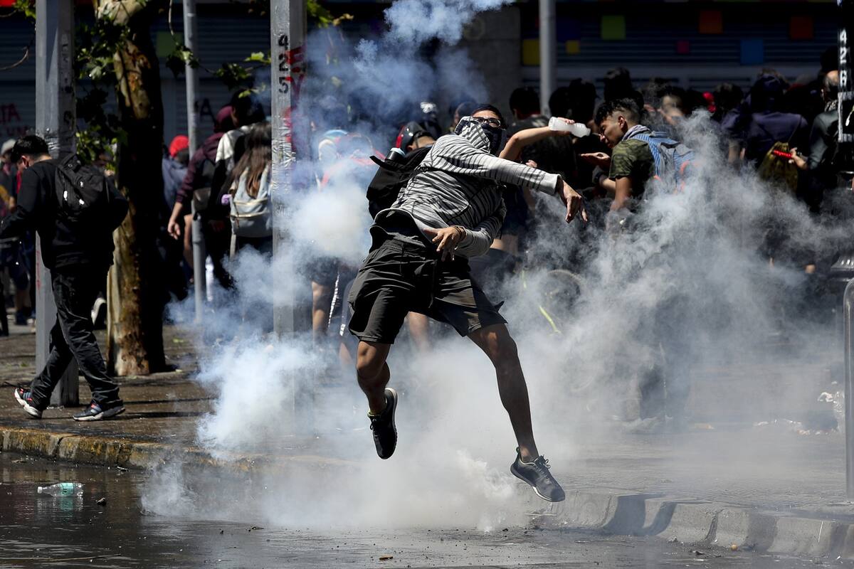 Un participante de las protestas le lanza de vuelta a la policía un cartucho de gas lacrimógeno