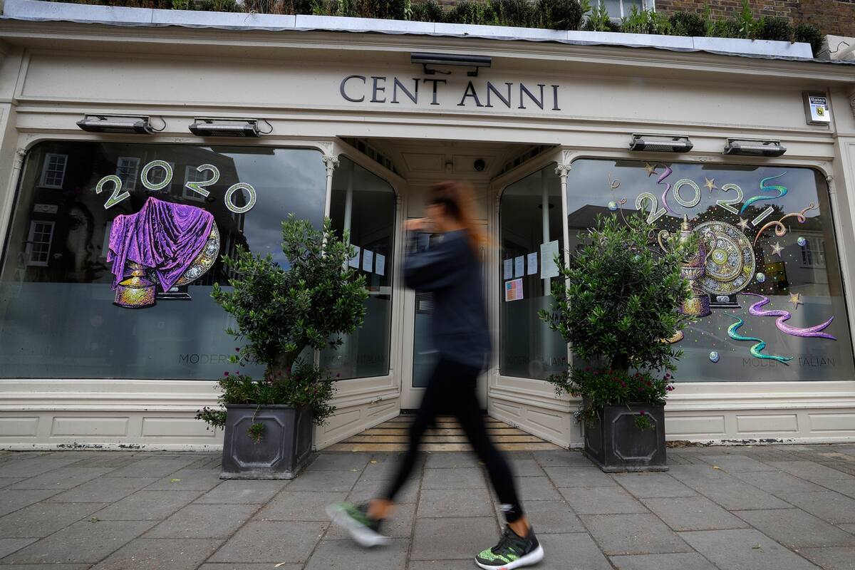 Un peatón pasa por un restaurante italiano cerrado que muestra los trofeos de los ganadores de Wimbledon en Wimbledon. El Campeonato de Tenis de Wimbledon 2020, que comenzaría el lunes, se canceló debido a la pandemia de Coronavirus.