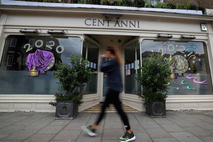 Un peatón pasa por un restaurante italiano cerrado que muestra los trofeos de los ganadores de Wimbledon en Wimbledon. El Campeonato de Tenis de Wimbledon 2020, que comenzaría el lunes, se canceló debido a la pandemia de Coronavirus.